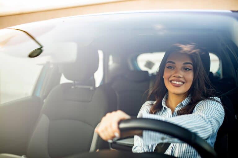 Beautiful young happy smiling woman driving her new car at sunset. Woman in car. Close up portrait of pleasant looking female with glad positive expression, woman in casual wear driving a car